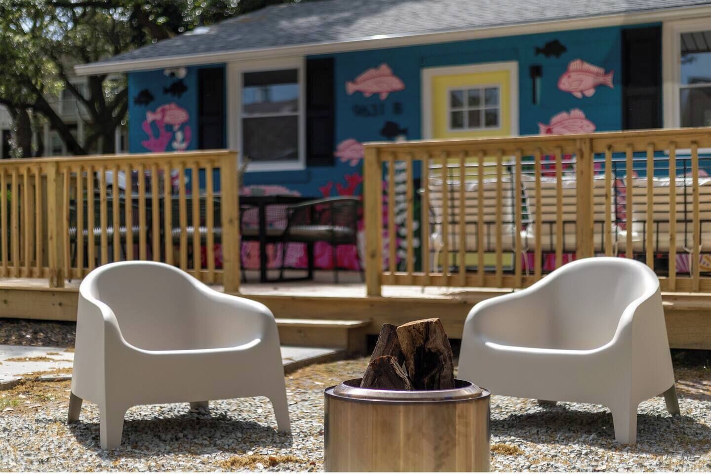 Een gebouw met een kleurrijke gevel, een houten terras en twee witte stoelen voor een vuurkorf.