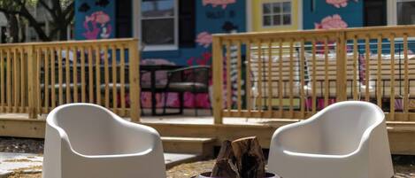 A building with a colorful exterior, a wooden deck, and two white chairs in front of a fire pit.
