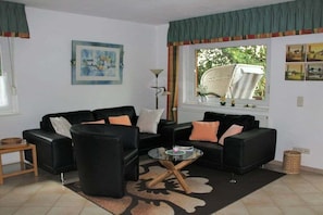 A living room with two black sofas, a glass coffee table, a floor lamp, and a window with a view of greenery. - Baltic Sea Life (Holiday Village House 29a) (Boltenhagen)