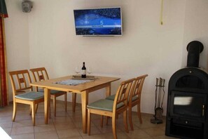 Un coin repas avec une table et des chaises en bois, un téléviseur fixé au mur et un poêle à bois noir.