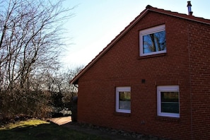 Une maison en briques rouges, avec un toit à pignon, deux fenêtres et une cheminée bien visible.