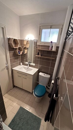 Ein kleines Badezimmer mit einem weißen Waschbecken, einer blauen Toilette und einem Fenster über der Toilette.