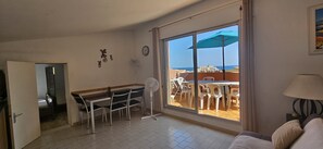 Una habitación con zona de comedor, un ventilador, un sofá y vista al mar a través de un ventanal grande.