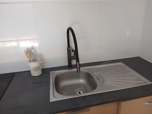 Una cocina con un lavamanos de acero inoxidable, un grifo negro y una taza blanca con utensilios.