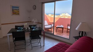 Ein Zimmer mit Esstisch, Stühlen, einem roten Sofa, einer Lampe und Meerblick durch ein großes Fenster.