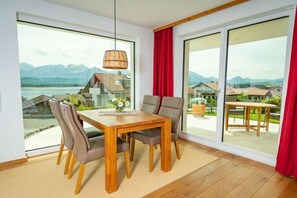 A dining area with a table and chairs, large windows with a view of mountains and a lake, and a hanging light fixture. - Holiday apartment with 2 bedrooms (Füssen)