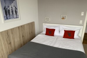 Ein Schlafzimmer mit einem hölzernen Kopfstück, weißer Bettwäsche und zwei roten Kissen.
