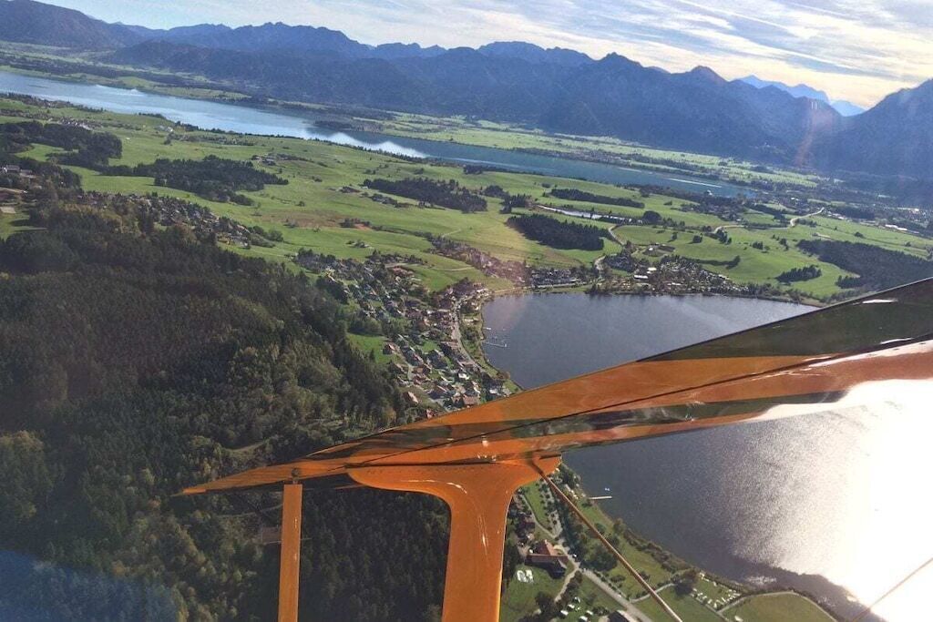 Eine Luftaufnahme einer Seenlandschaft mit einer kleinen Siedlung und Bergen im Hintergrund.