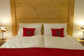 A double bed with white bedding and two red pillows with a deer design, flanked by nightstands with lamps. - Holiday apartment with 2 bedrooms (Füssen)
