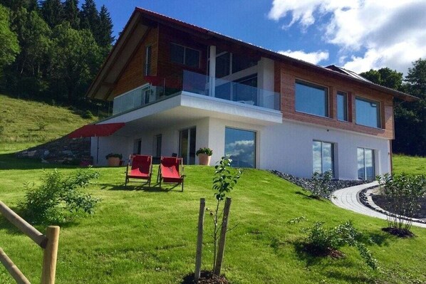 A modern two-story house with a balcony, a lawn, and a red chair. - Holiday apartment with 2 bedrooms (Füssen)