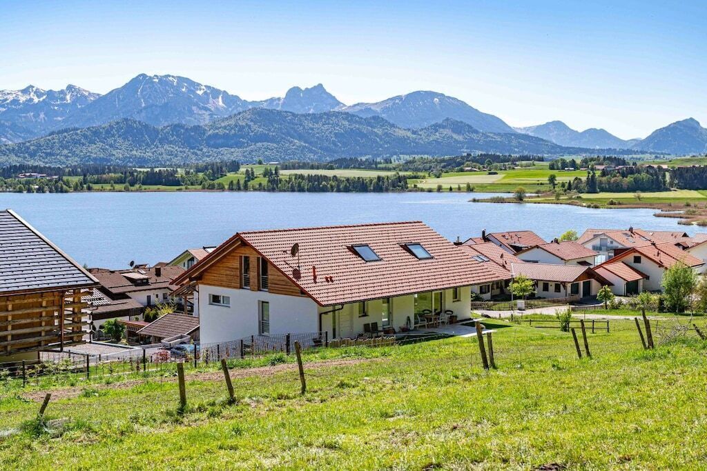 Ein Dorf am See mit Häusern, einer Holzhütte und Bergen im Hintergrund.