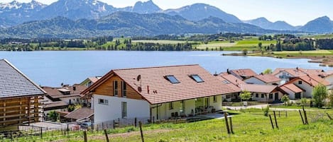 A lakeside village with houses, a wooden cabin, and mountains in the background.
