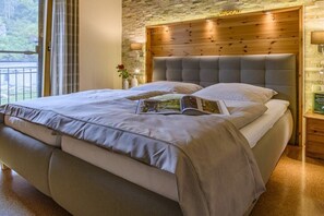 Un dormitori amb un llit gran, un panell de capçal de fusta, una tauleta de nit amb una làmpada i vista a l'exterior.