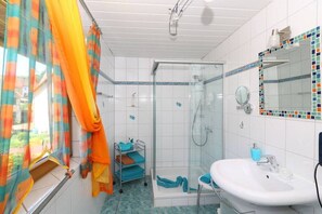 Un bany amb dutxa de vidre, un lavabo blanc i una zona de dutxa amb rajola.