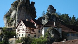 A traditional half-timbered house with a steeply pitched roof, situated on a hillside with rocky outcrops. - Holiday home with 2 bedrooms (Waischenfeld)