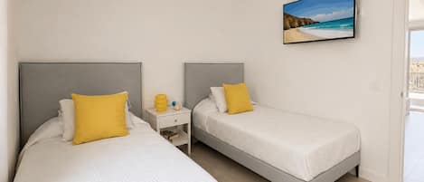 A hotel room with two beds, a nightstand, a painting, and a view of the sea.