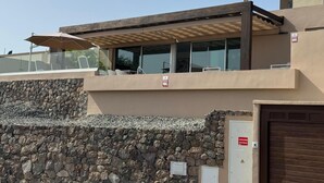 Un edificio moderno con un muro de piedra, una zona de estar al aire libre techada y una entrada con portón.
