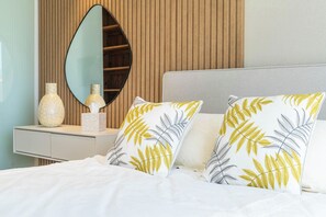 A neatly made bed with white bedding, a bedside table with a vase and a tissue box, and a large mirror on the wall. - Kaiman 19 by VillaGranCanaria (San Bartolomé de Tirajana)