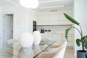 A modern kitchen with white cabinets, a coffee machine, and a dining area with a glass table and chairs. - Kaiman 19 by VillaGranCanaria (San Bartolomé de Tirajana)