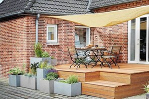 A brick house with a wooden deck, a table and chairs, and planters with greenery. - Holnis Customs House (Glücksburg)