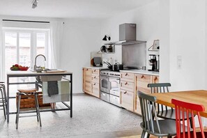 A modern kitchen with a central island, stainless steel appliances, and a dining area with mismatched chairs. - Holnis Customs House (Glücksburg)