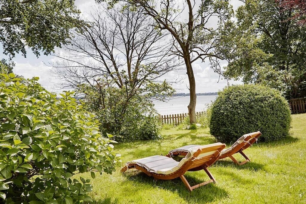A garden with two wooden lounge chairs and a view of a body of water.
