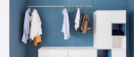 Una habitación con pared azul, suelo de madera, armario blanco y ropa colgada en una barra.