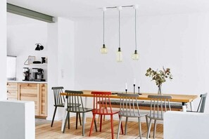 Eine moderne Küche mit einem Holzespeisetisch und Stühlen, einer Kaffeemaschine und einer Vase mit Blumen.
