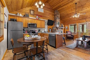 A log cabin-style kitchen with wooden cabinets, a refrigerator, microwave, and a dining area with a table and chairs.