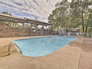 A swimming pool with a stone wall and a covered area with tables.