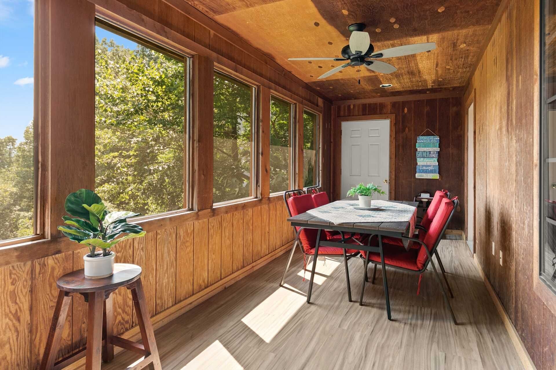 A wooden-paneled room with a table and chairs, large windows, and a ceiling fan.