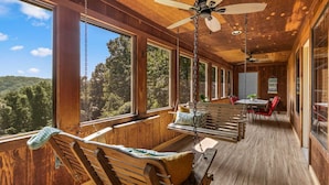 A wooden cabin with a porch, large windows, a ceiling fan, and a dining area.