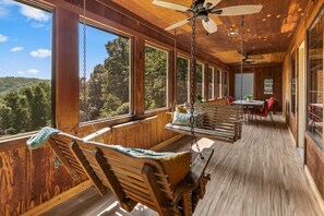 Eine Holzhütte mit einer Veranda, großen Fenstern, einem Deckenventilator und einem Essbereich.