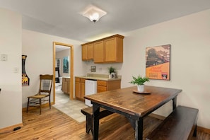 A compact kitchen with wooden cabinets, a dining table, and a bench.