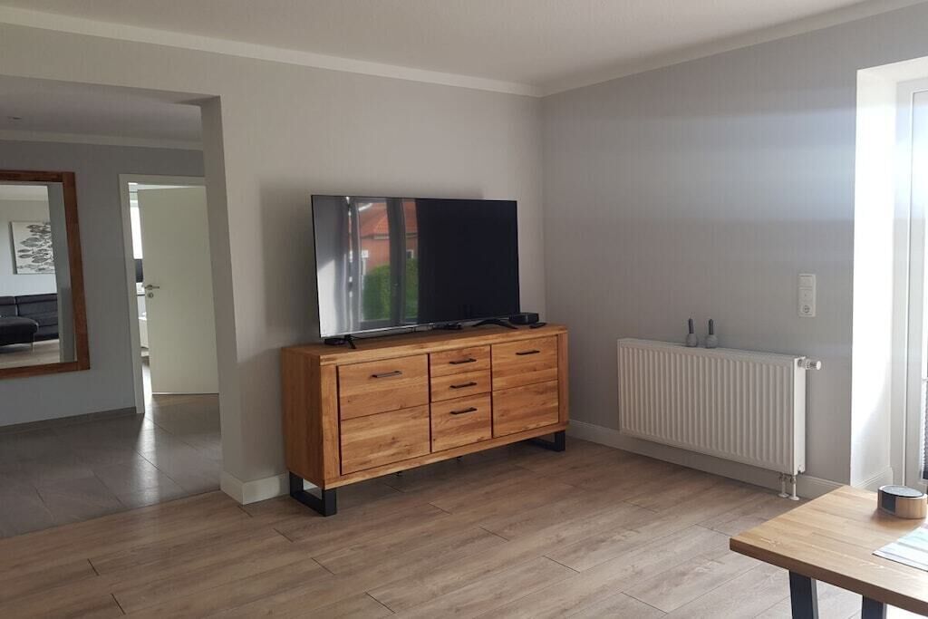 A room with a wooden cabinet, a flat-screen TV, a radiator, and a wooden table.