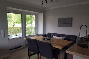 Een moderne eetruimte met een houten tafel, donkere stoelen en een bank. Er is een glazen deur die naar een buitenruimte leidt.