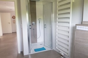 Een douchecabine met glazen wanden, een handdouche, een handdoek op de vloer en een witte radiator.