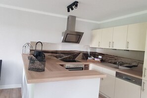 A modern kitchen with a central island, built-in oven, stainless steel range hood, and light-colored cabinets. - Herring in the Fisherman's House (Hohwacht)