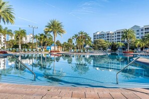 A swimming pool with lounge chairs, palm trees, and hotel buildings in the background. - Orlando | Orlando Resort Stay | Pool & Water Park | 2BR (Orlando)
