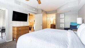 Ein Hotelzimmer mit einem großen Bett, einem Holzkonsolenmöbel, einem Flachbildfernseher, einem Deckenventilator und einem durchgehenden Türspalt einsehbarer Badezimmer.