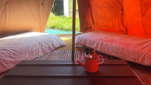 Ein Zelt mit zwei Betten, einem Fenster und einer roten Wasserkaraffe auf einer Matte.