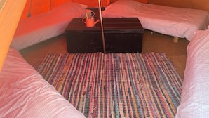 Ein Zelt mit zwei Betten, einem kleinen Tisch und einem farbenfrohen Teppich.
