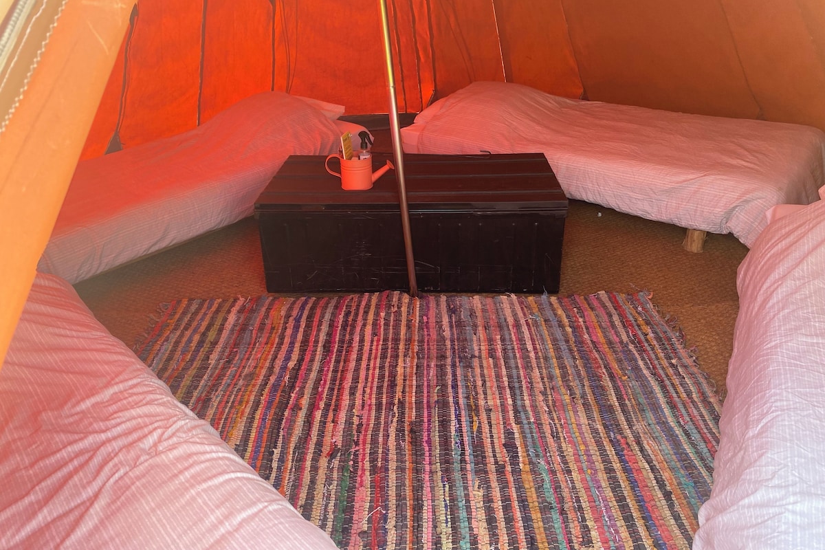 Una tenda con due letti, un tavolino e un tappeto colorato.