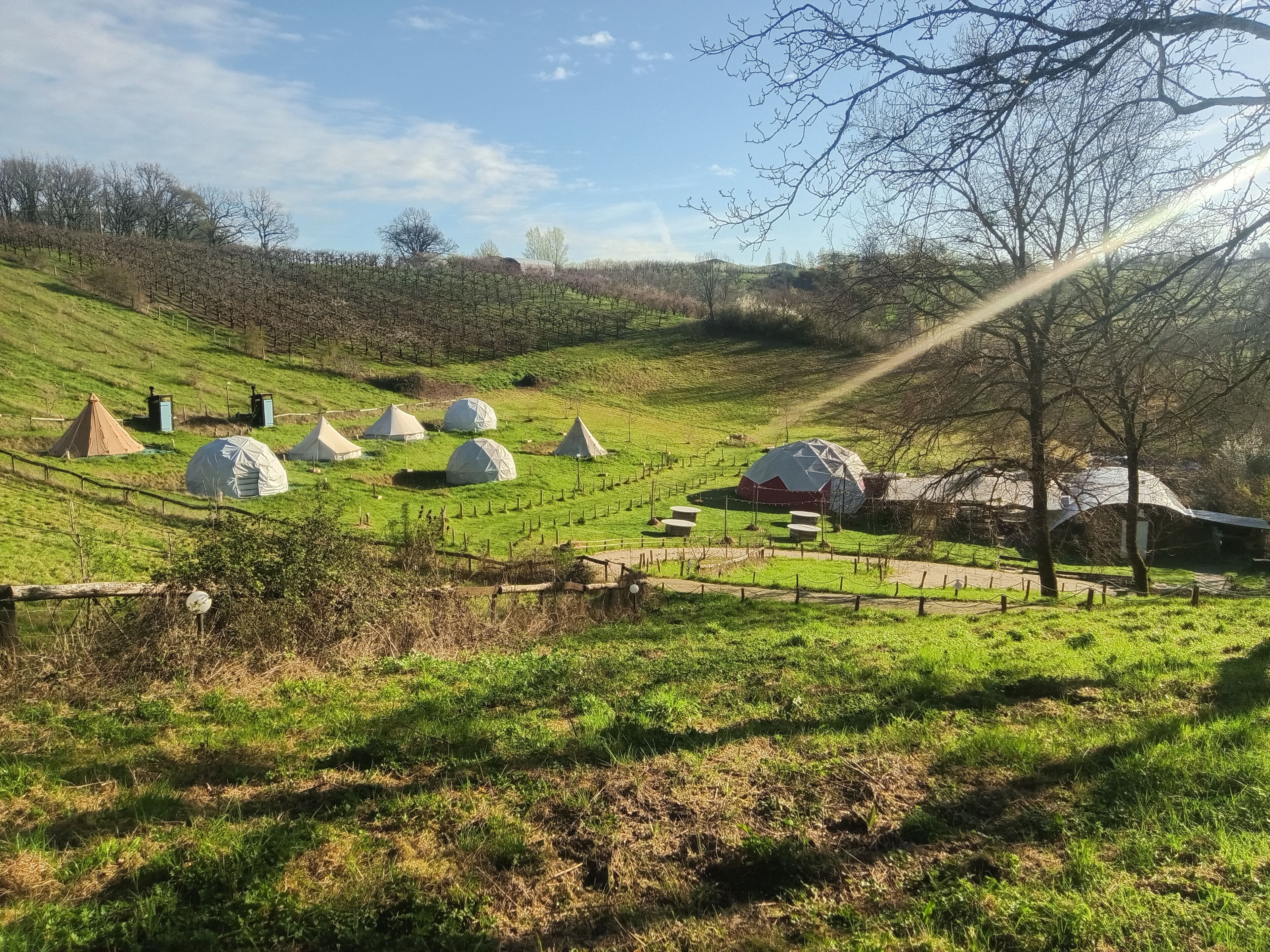 Een landelijk landschap met meerdere geodetische koepelstructuren, een rode schuur en een omheind gebied met paden.