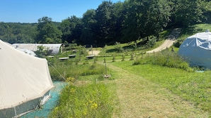 Un terrain de camping avec des tentes, un petit plan d’eau et un sentier de terre.