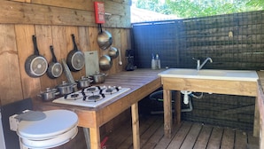 Eine Außenküche mit Gaskochfeld, Töpfen, Pfannen, Spüle und Toilette.