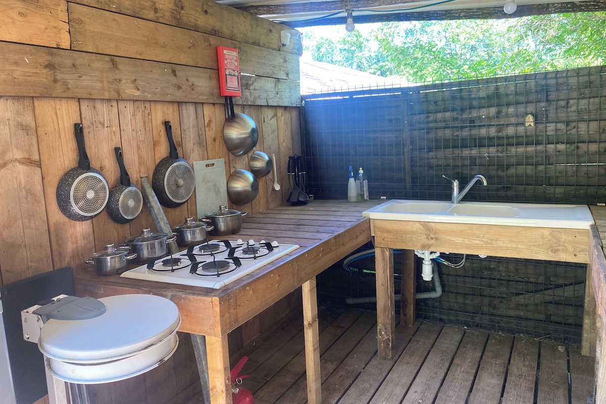 Una cucina esterna con piano cottura a gas, pentole, padelle, lavello e un WC.