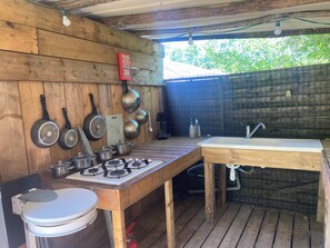 Una cucina esterna con piano cottura a gas, pentole, padelle, lavello e un WC.