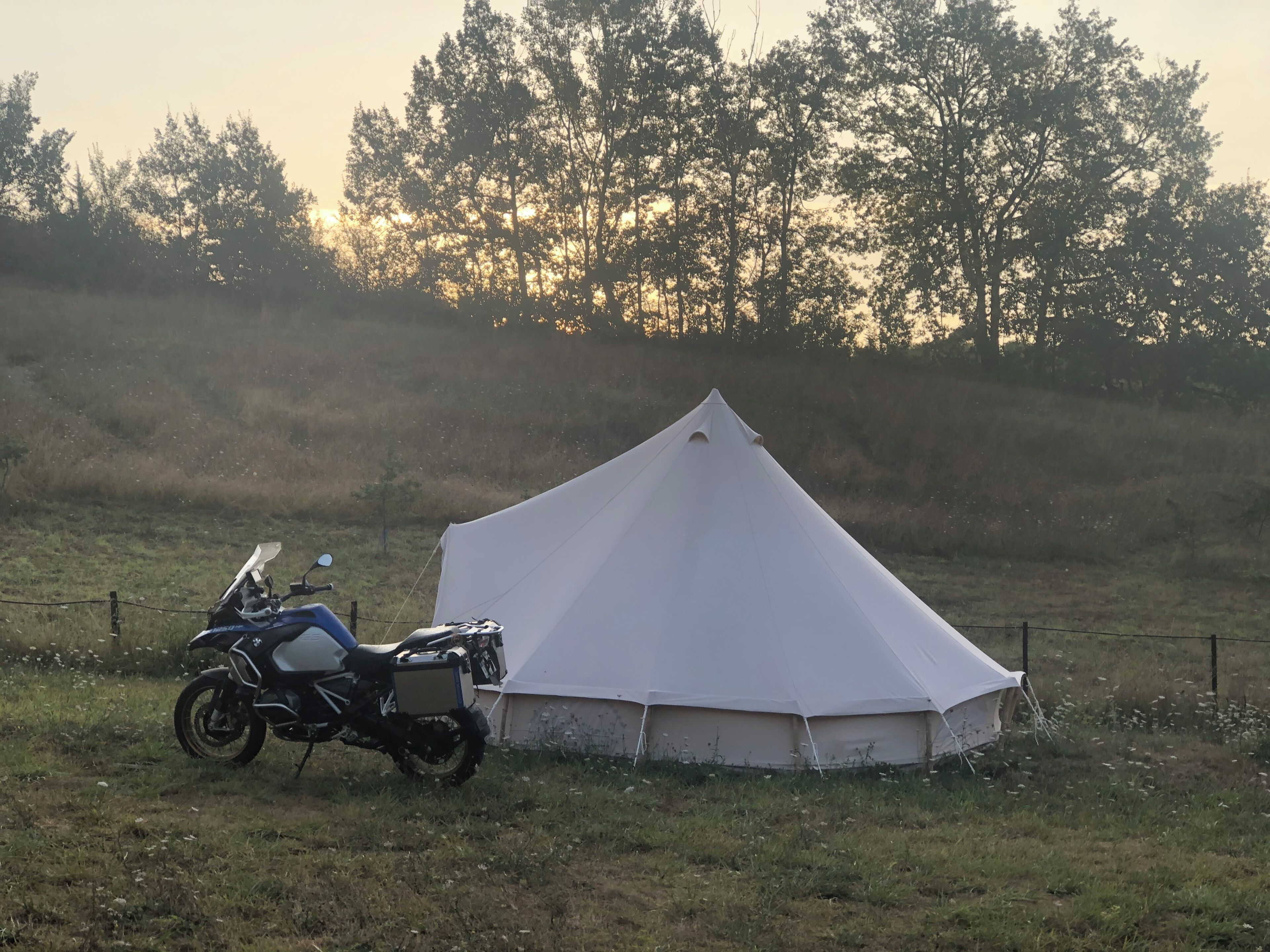Ein Zelt mit einem Motorrad, das daneben geparkt ist, in einem grasbewachsen Feld.
