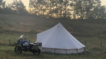 Ein Zelt mit einem Motorrad, das daneben geparkt ist, in einem grasbewachsen Feld.